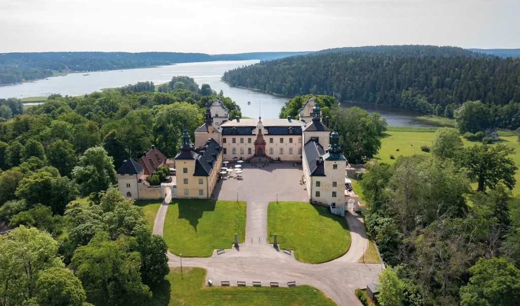 Stort pampigt slott framför en fjärd och skog.