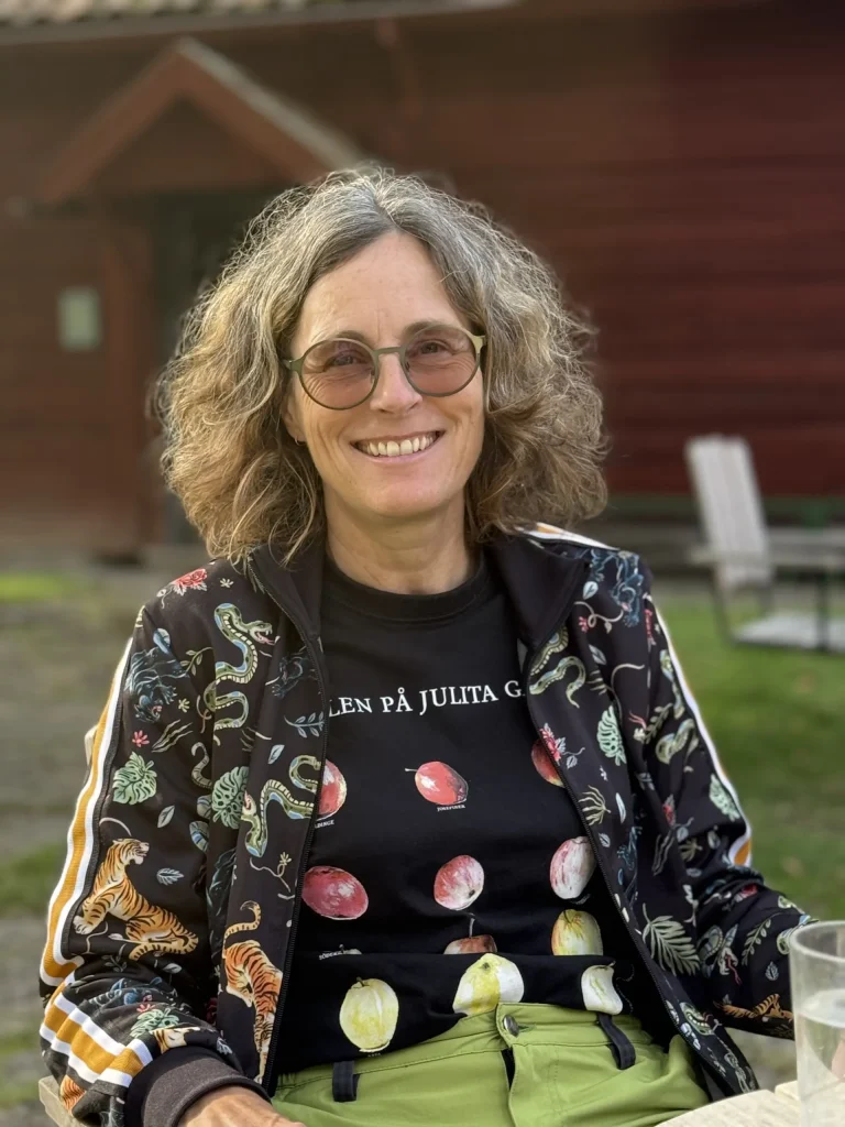 En kvinna i tonade glasögon, klädd i svart t-shirt med äpplen på står utomhus