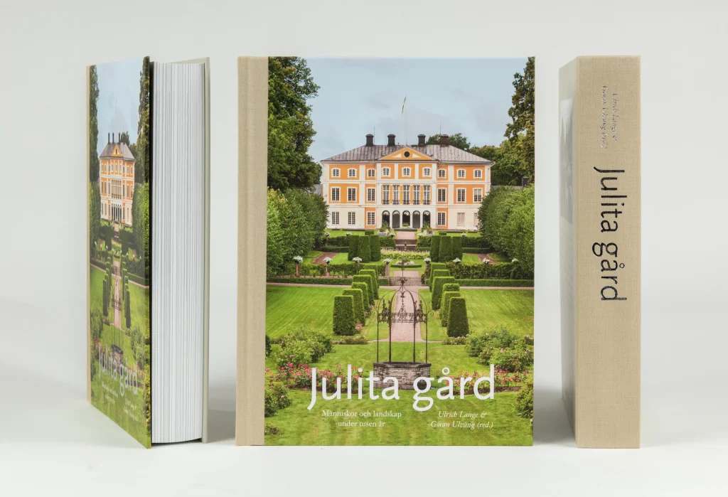 Tre av samma tjocka bok med Julita gård på omslaget står uppställda mot en ljus bakgrund.