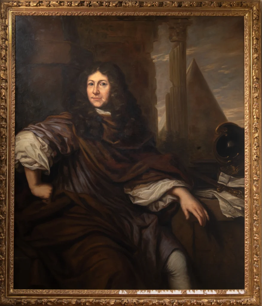 En målning med ram med en man i lång brun peruk och draperad mörk klädsel sitter med ena handen i sidan och intensiv blick och ett litet leende mot betraktaren.