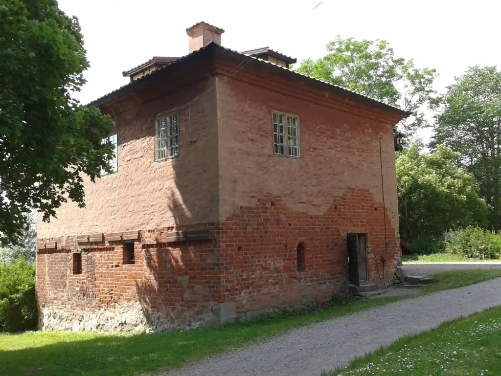 Ett äldre klosterhus i tegel omringat av natur.