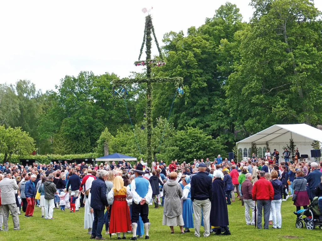 En stor samling människor vid en midsommarstång och en scen med spelmän.