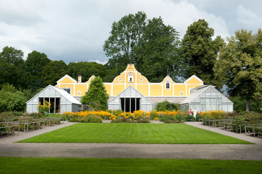 En gul byggnad med tre glasade växthus och planteringar framför.