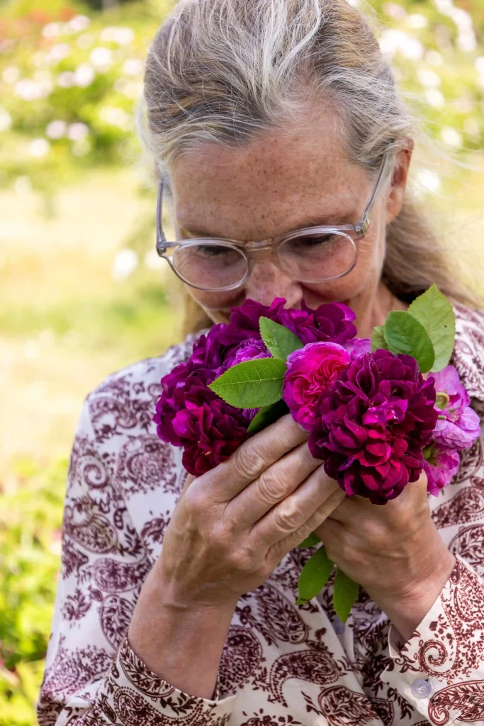 En kvinna i blommig blus doftar på en vinrödlila blomma