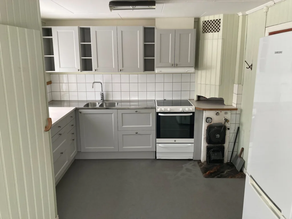 Ett kök med grå luckor, vitt kakel, vedspis, modern spis och skafferi.