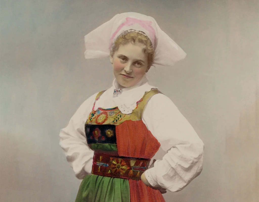 Ett kolorerat fotografi en kvinna i folkdräkt med händerna i sidorna