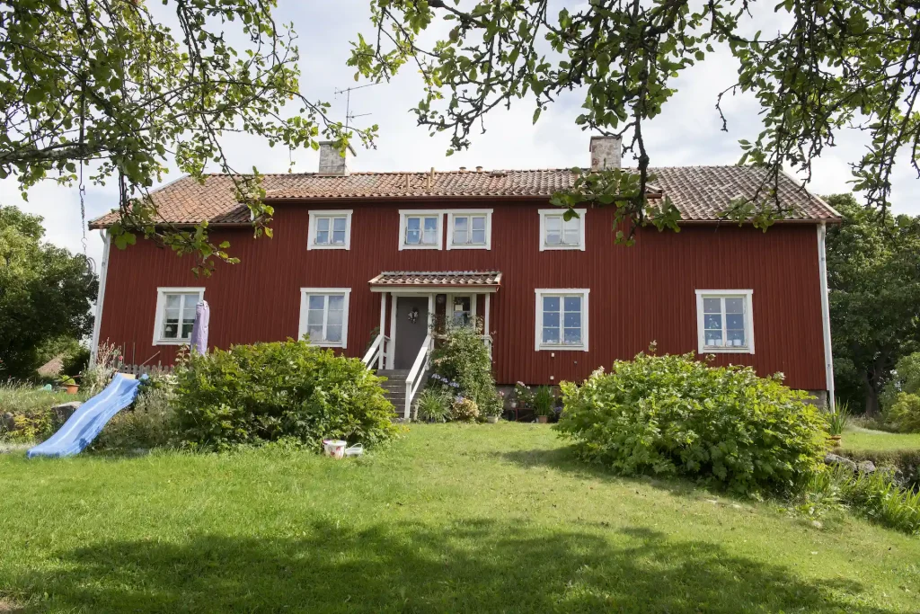 En faluröd länga med buskar och gräsmatta framför, en blå liten rutschkana till vänster